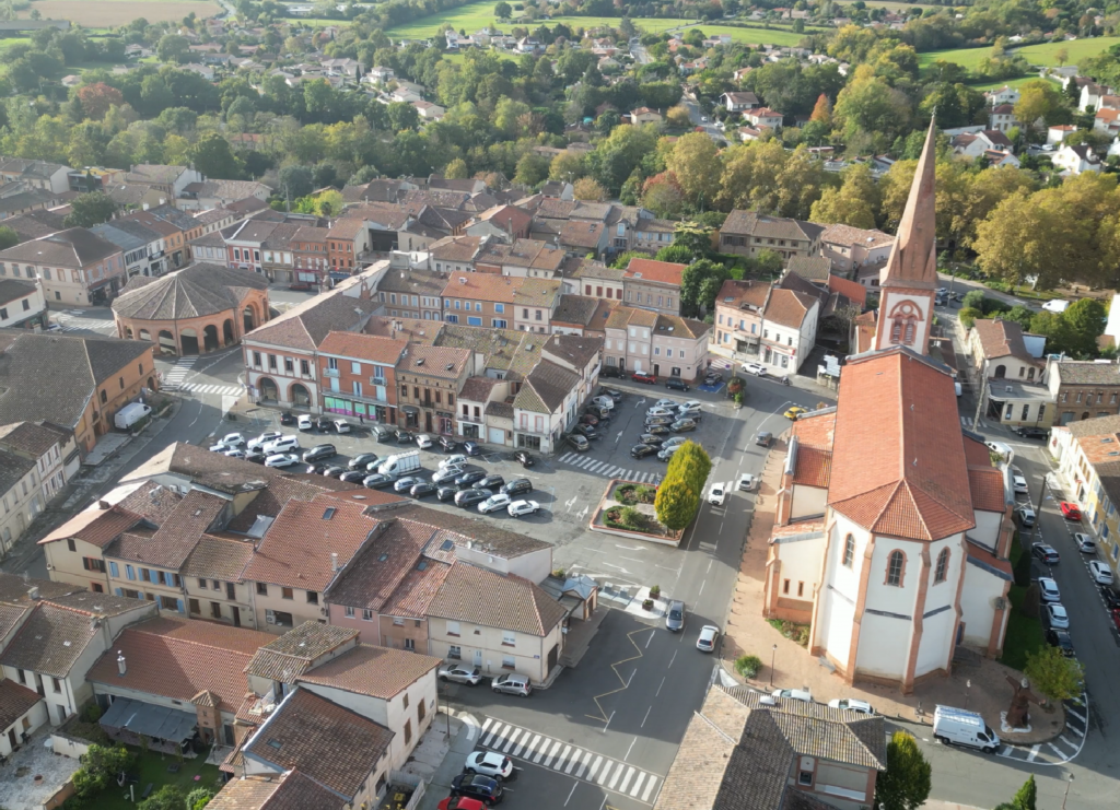 Vue aérienne par drone du centre-ville de Saint-Lys avec l’église, la place centrale et les commerces locaux.